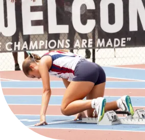 Female track athlete kneeling at blocks.